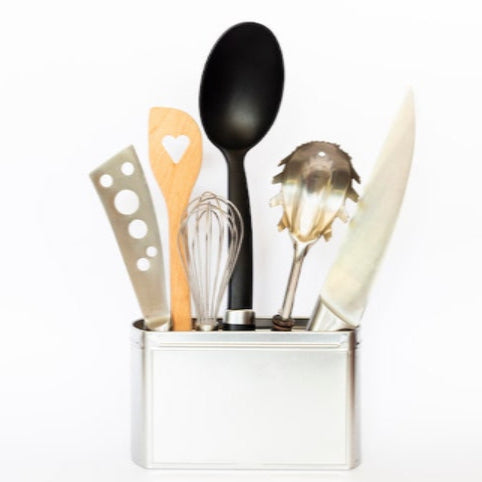 Set of kitchen utensils including a black spoon, wooden spatula, whisk, and others in a holder on a white background.